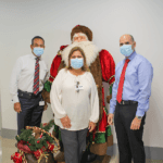 A woman and two men posing in front of a santa clause