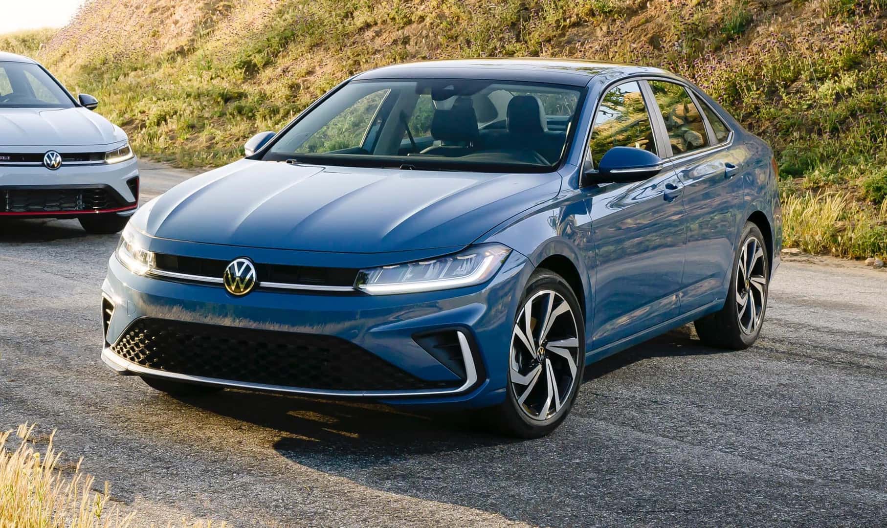 The Affordable And Reliable Volkswagen Jetta, Parked On A Concrete Road With Another Volkswagen Jetta Parked In The Corner Of The Pic