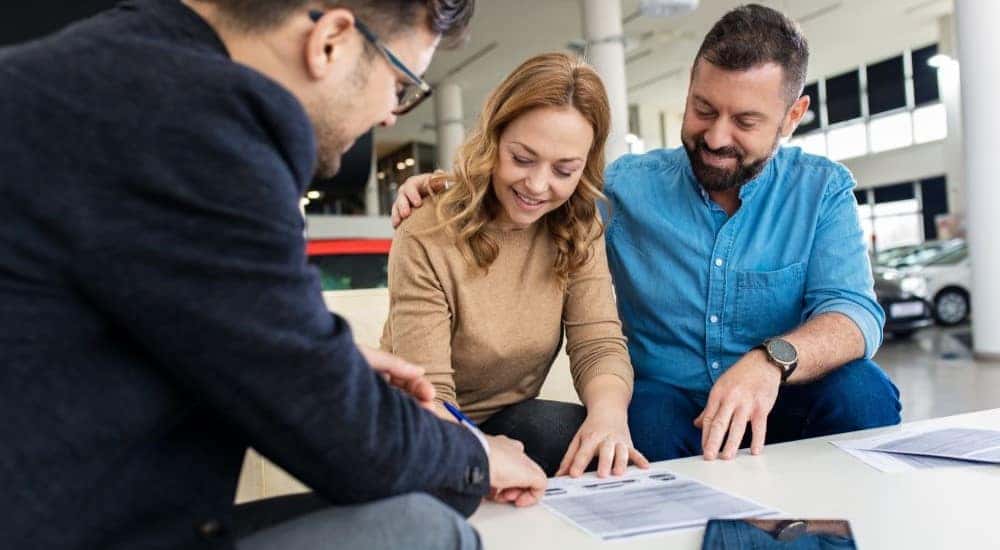 A smiling couple is shown signing paperwork at a dealership.