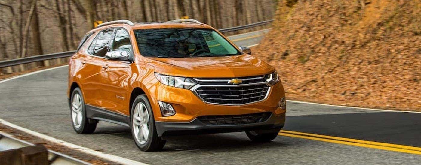 An orange 2018 Chevy Equinox is shown driving to a used Chevy dealership.