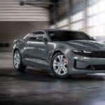 A grey 2022 Chevy Camaro LS is shown driving through a warehouse at a Chevrolet dealer.