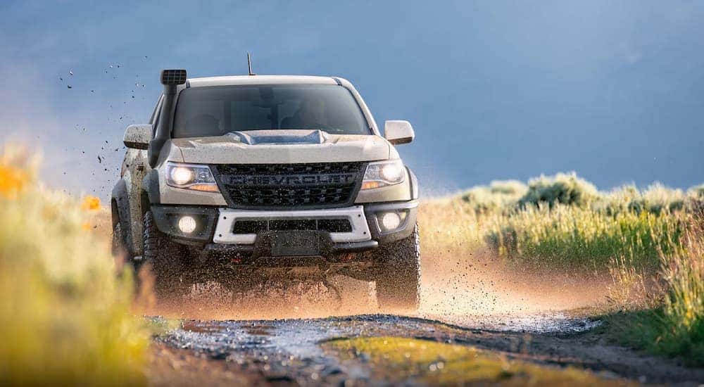 A tan 2022 Chevy Colorado ZR2 is shown from the front while driving on a muddy road.