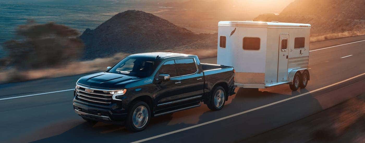 A black 2022 Chevy Silverado 1500 High Country is shown towing a horse trailer.