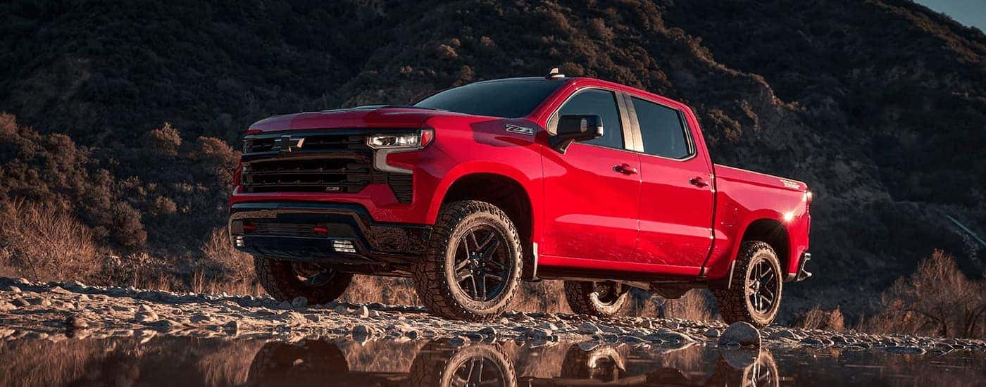 A red 2023 Chevy Silverado 1500 Z71 is shown parked on rocked next to a small pond.