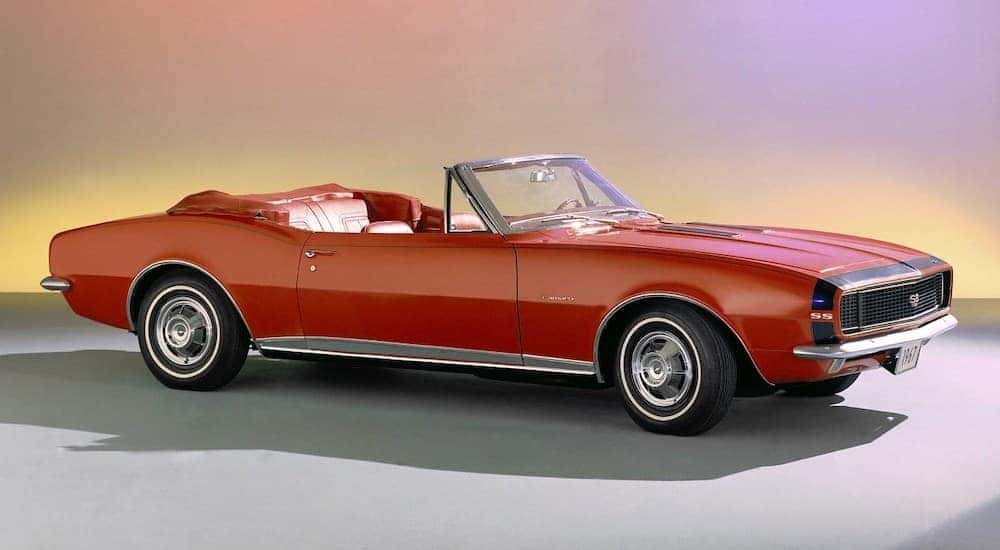 A red 1966 Chevy Camaro is shown parked on a showroom floor.