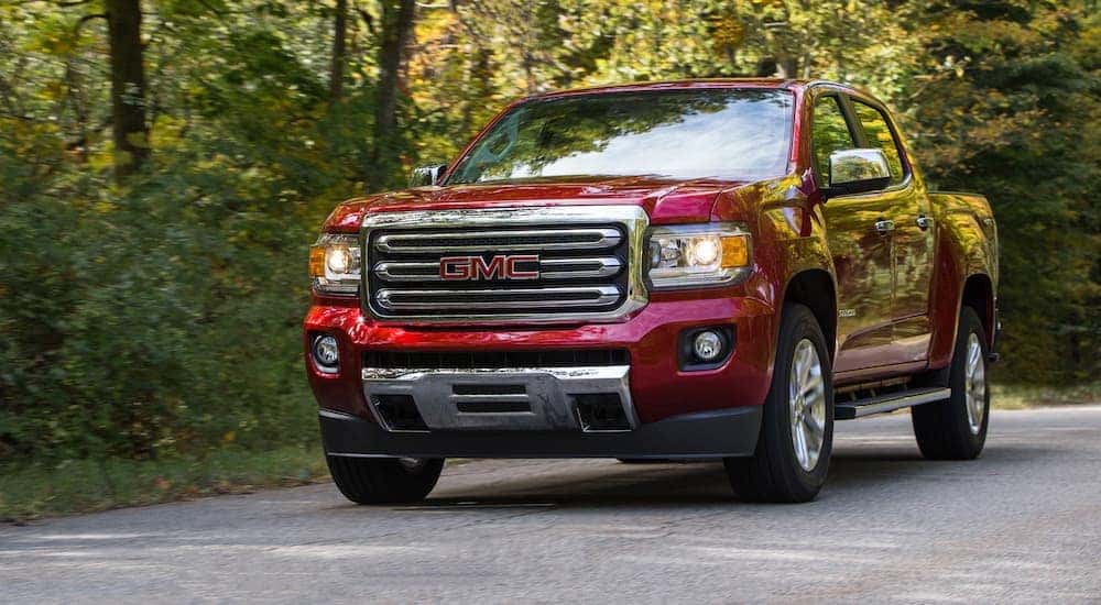 A red 2019 GMC Canyon SLT is shown on a tree-lined road after looking at used trucks for sale.