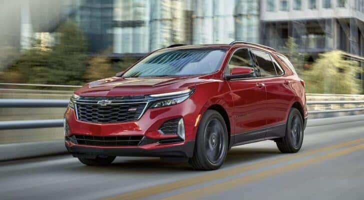 A red 2023 Chevy Equinox RS is shown driving on a city street after viewing used Chevy SUVs for sale.