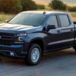 A popular used Chevy Silverado for sale, a black 2021 Chevy Silverado 1500 LT, is shown driving on a highway.