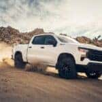 A white 2024 Chevy Silverado 1500 Custom Trail Boss kicking up dust while off-roading.