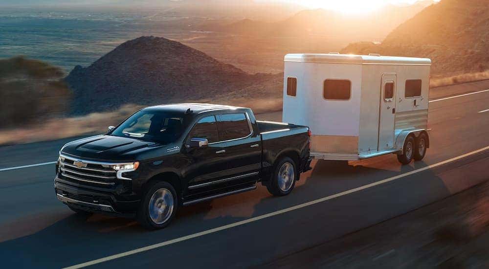 A black 2024 Chevy Silverado 1500 High Country towing a trailer on a mountain road.