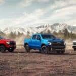 Three 2024 Chevy Silverado 1500s, different trims and colors, parked in front of snow-capped mountains.