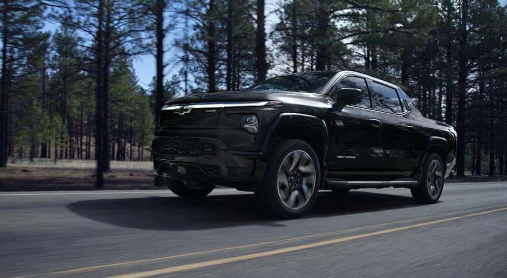 A black 2024 Chevy Silverado EV is driving on a tree-lined road.