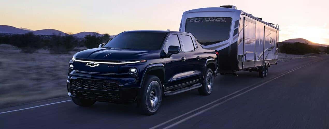 A black 2024 Chevy Silverado EV RST towing a large camper.