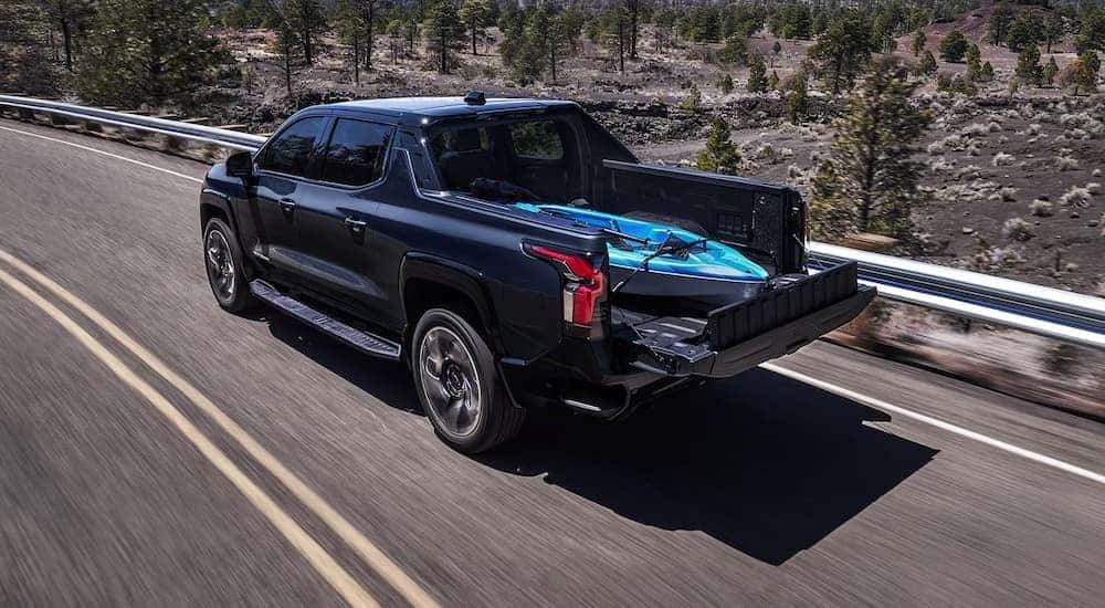 A black 2024 Chevy Silverado EV RST is driving on a highway with a kayak in the bed.