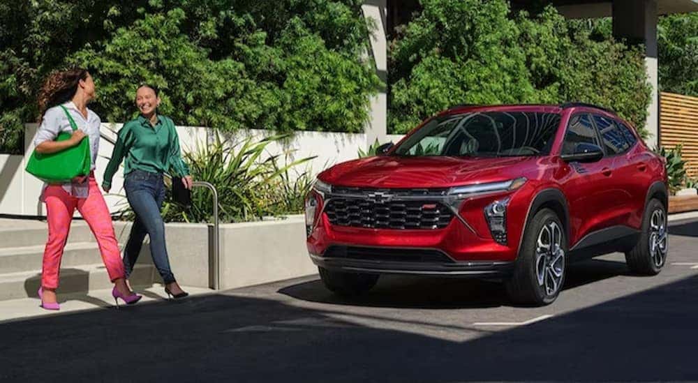 A red 2024 Chevy Trax RS is shown parked near two people walking.