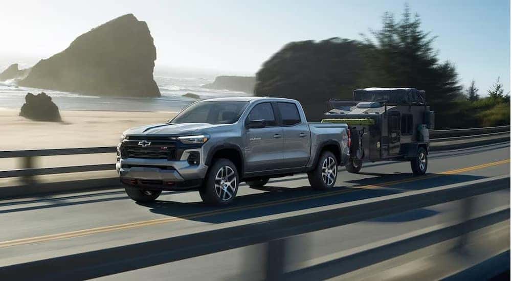 A popular Chevy Colorado for sale, a silver 2024 Chevy Colorado Z71, is shown towing a trailer on a highway.