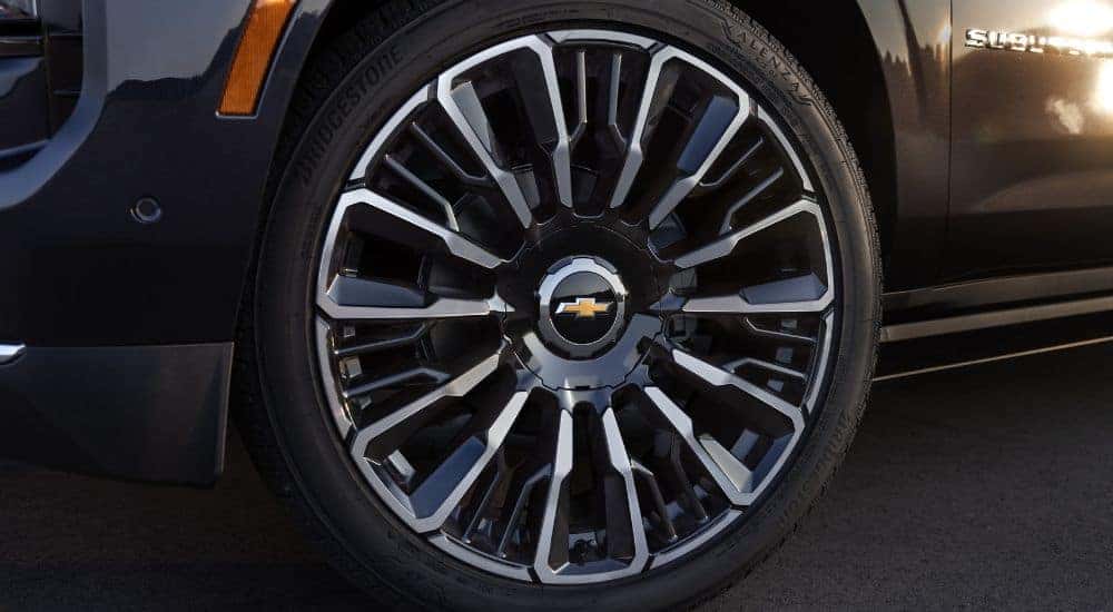 A close-up shows the front driver side wheel on a black 2025 Chevy Suburban High Country.