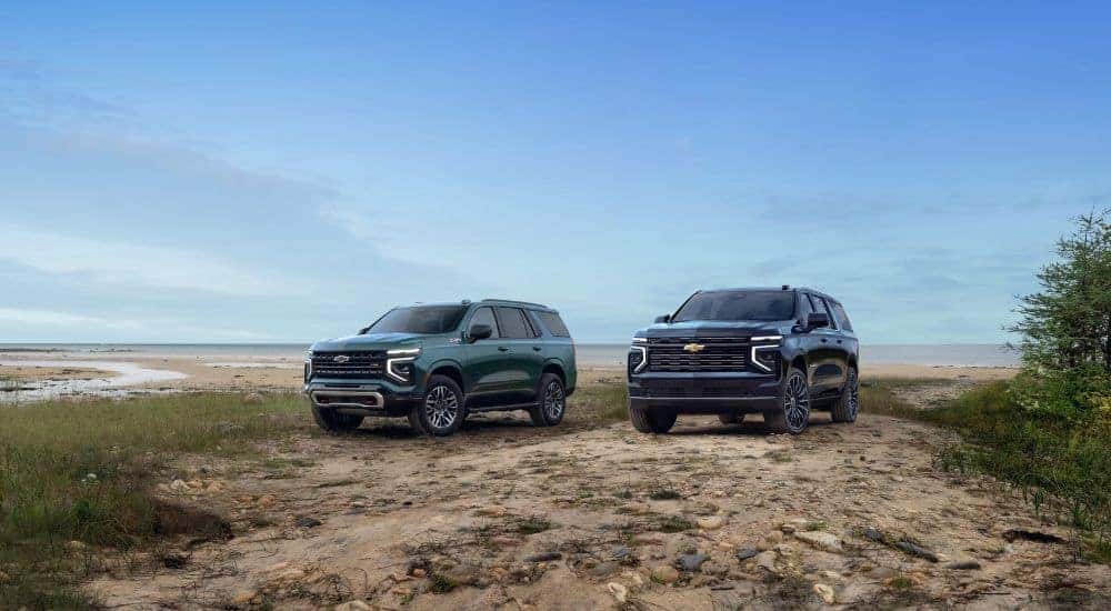 A green 2025 Chevy Tahoe Z71 and a blue Suburban High Country are shown off-road.