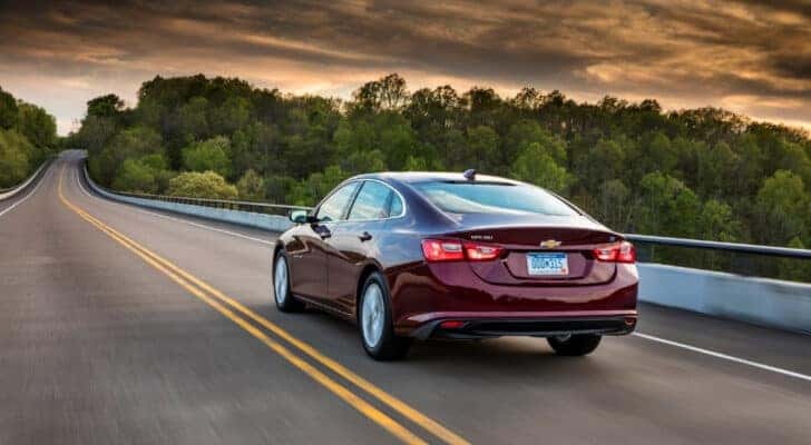 A purple 2018 Chevy Malibu is shown from the rear driving on a cloudy day.