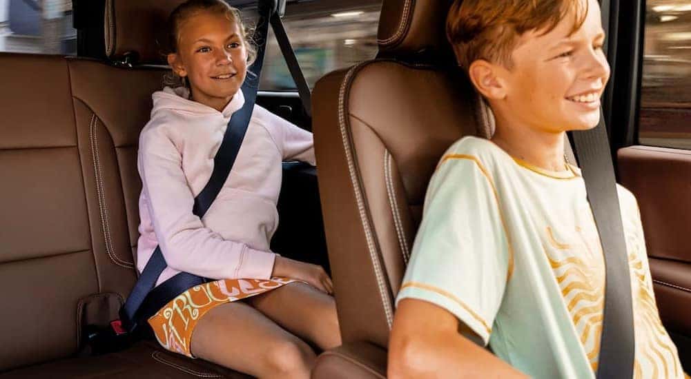 Two children are shown sitting in the brown rear seating area of a 2025 Chevy Suburban.