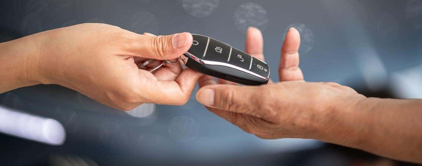 A car salesman is handing a key to a customer.