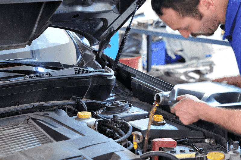 Person pouring fresh motor oil into a vehicle engine during an oil change service