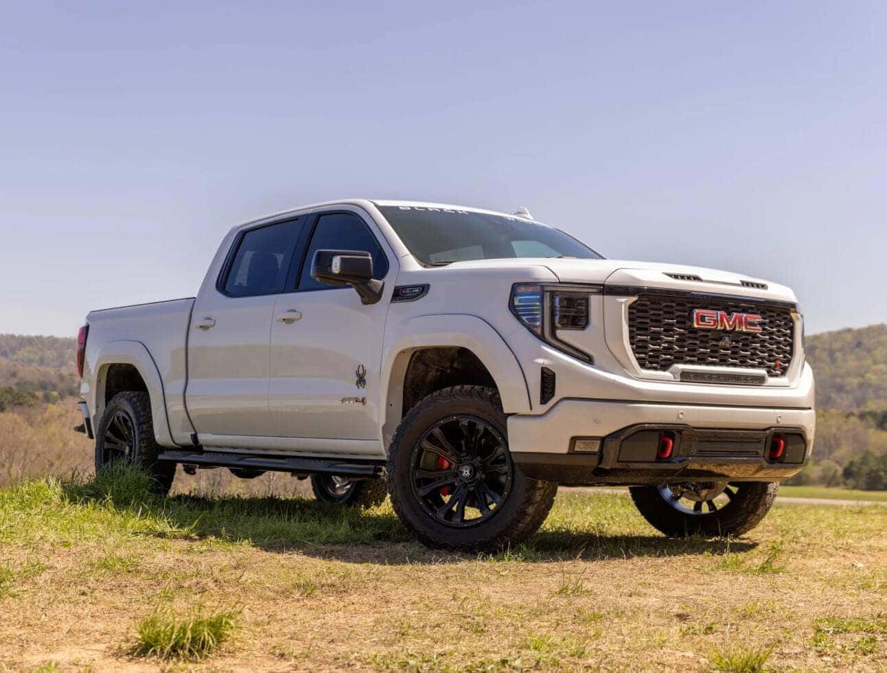 Low-angle front three-quarter view of white GMC Sierra 1500 Black Widow parked on a grassy hill.