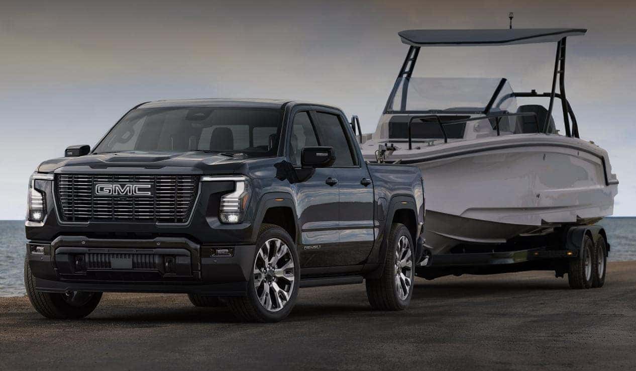 2027 GMC Sierra 1500 towing a large boat on a trailer near the water.