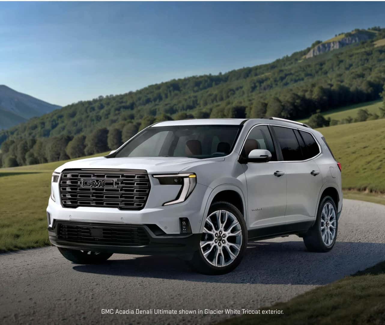 Front three-quarter view of a 2027 GMC Acadia Denali Ultimate in Glacier White Tricoat parked on a gravel country road.