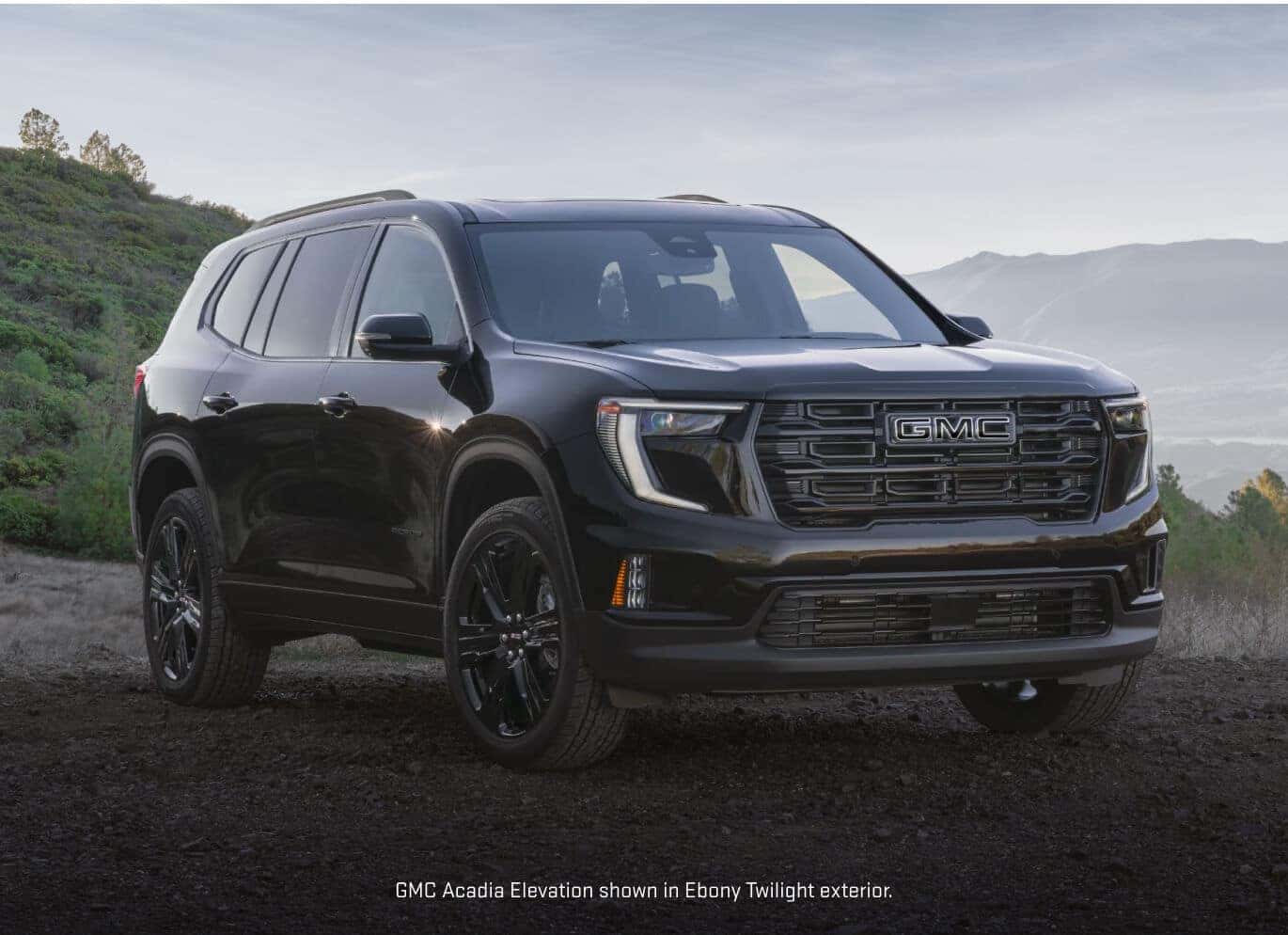 Front three-quarter view of a 2027 GMC Acadia Elevation in Ebony Twilight Metallic parked on a gravel trail.