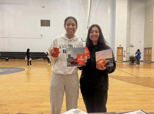 2 high school girls holding up Vaden merch in basketball courts