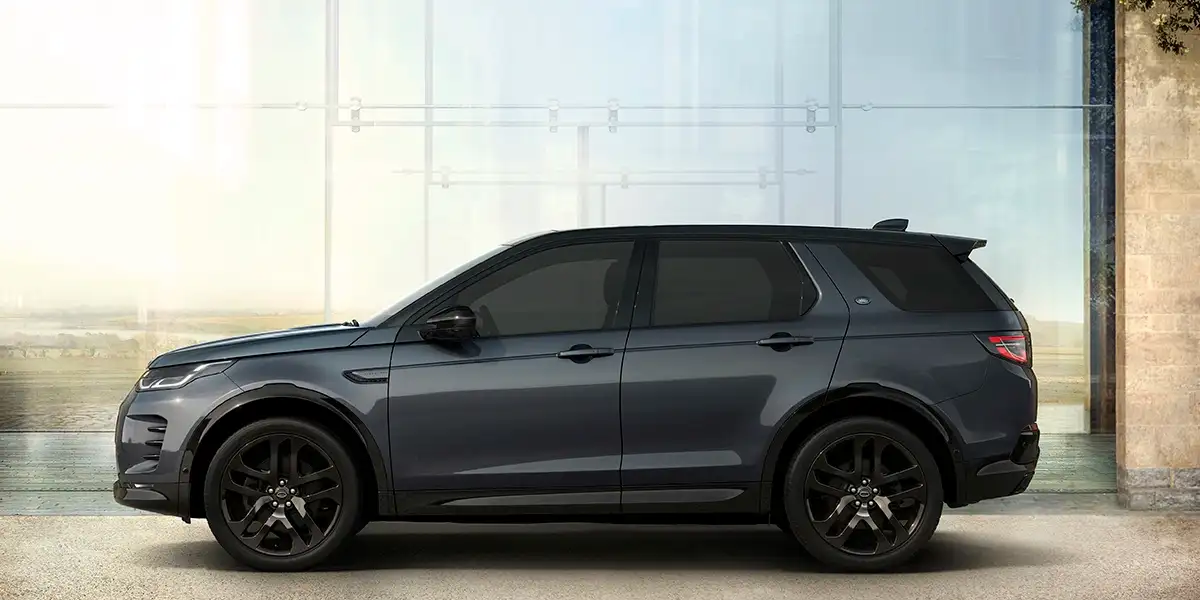 Passenger side profile of 2026 Land Rover Discovery Sport Dynamic HSE parked outside modern architecture.