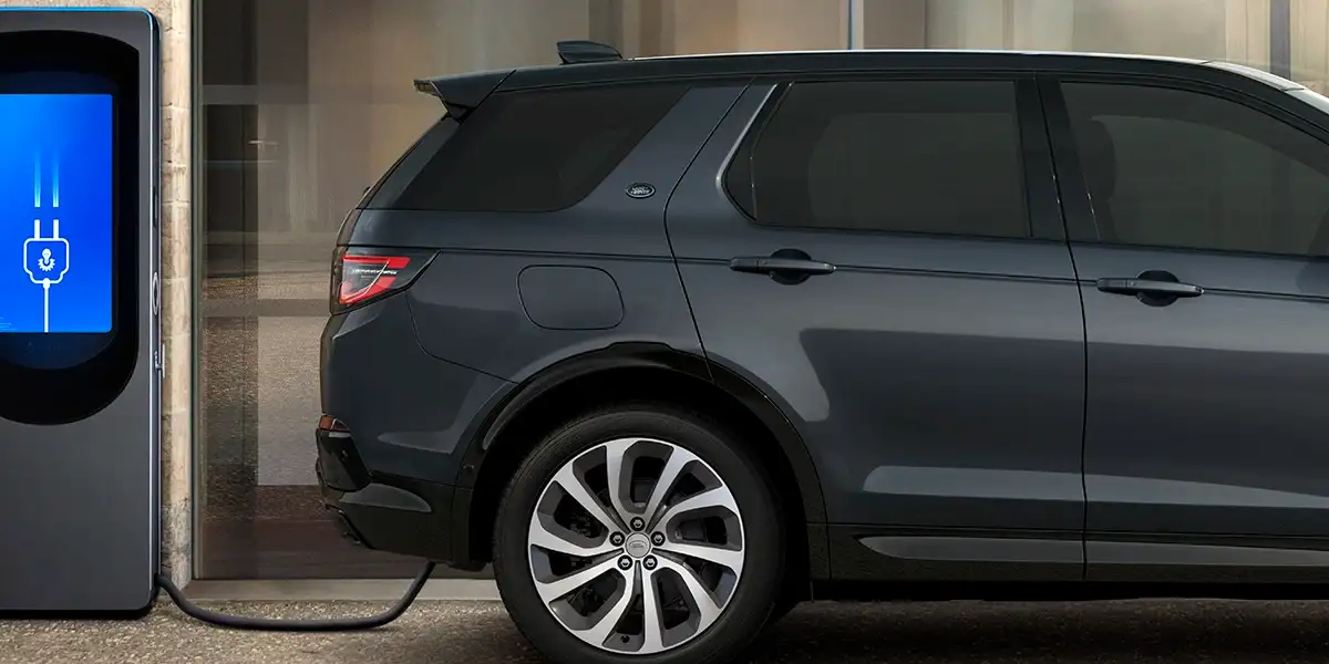 2026 Land Rover Discovery Sport Plug-in Hybrid charging at a station, showcasing efficiency and modern design.