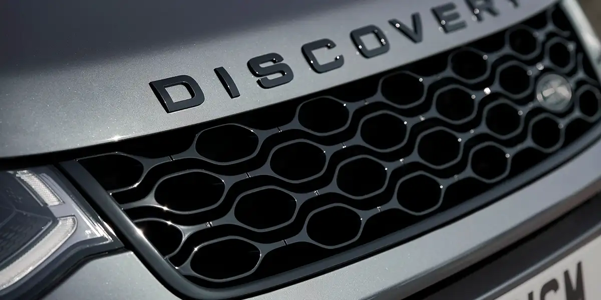 Close-up of 2026 Land Rover Discovery Sport grille with DISCOVERY lettering and gloss black accents.