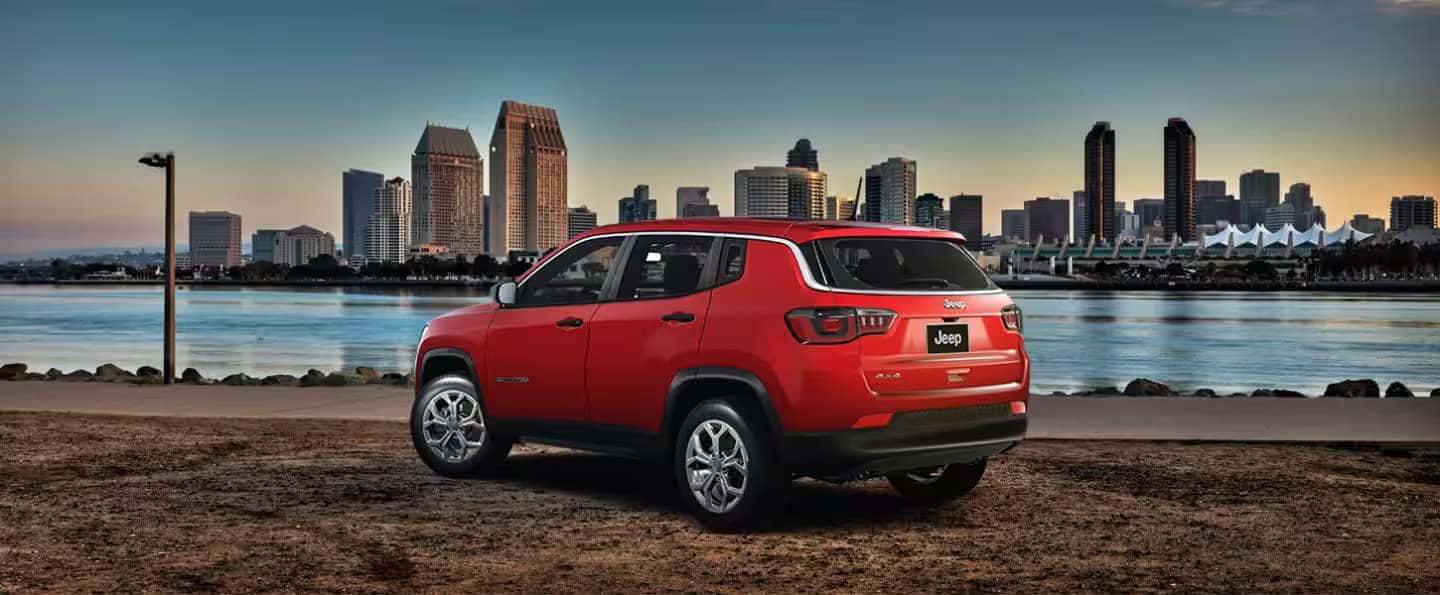 Rear exterior view of the 2024 Jeep Compass in red, parked near a city waterfront