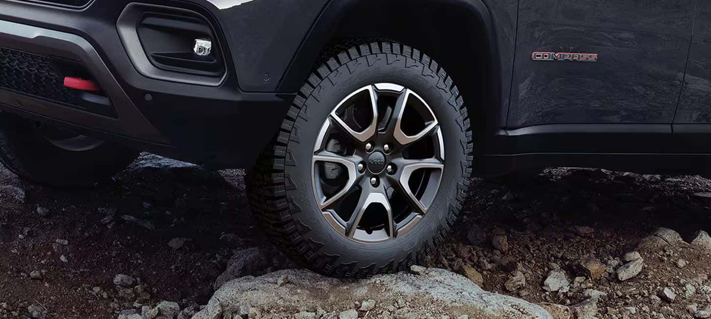 Close-up view of the 2024 Jeep Compass wheel on a rocky off-road terrain