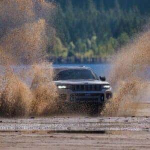 Jeep Grand Cherokee splashing through muddy terrain by a lake showcasing off-road capabilities.