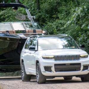Jeep Grand Cherokee towing a large boat through a wooded path showcasing impressive towing capacity.