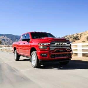 a red 2025 ram 2500 driving next to a white picket fence with a desert mountain background