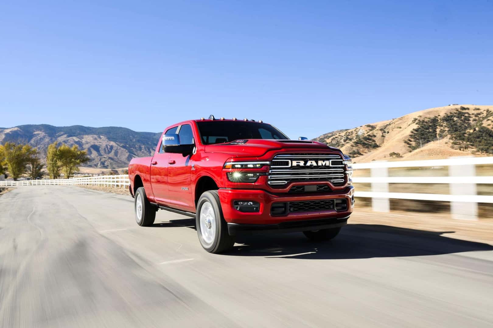 a red 2025 ram 2500 driving next to a white picket fence with a desert mountain background