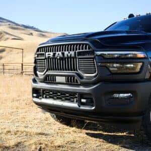 the front grille, headlights, and front driver's tire of a black ram 2500 parked in a dead grassy field.