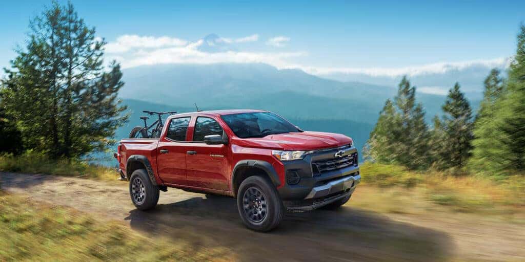2024 Chevrolet Colorado in red, driving through a scenic mountain area, highlighting its rugged exterior design.