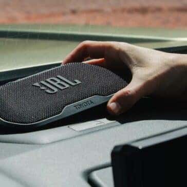 A JBL portable speaker being placed on the dashboard of a Toyota Tacoma, demonstrating premium audio features.