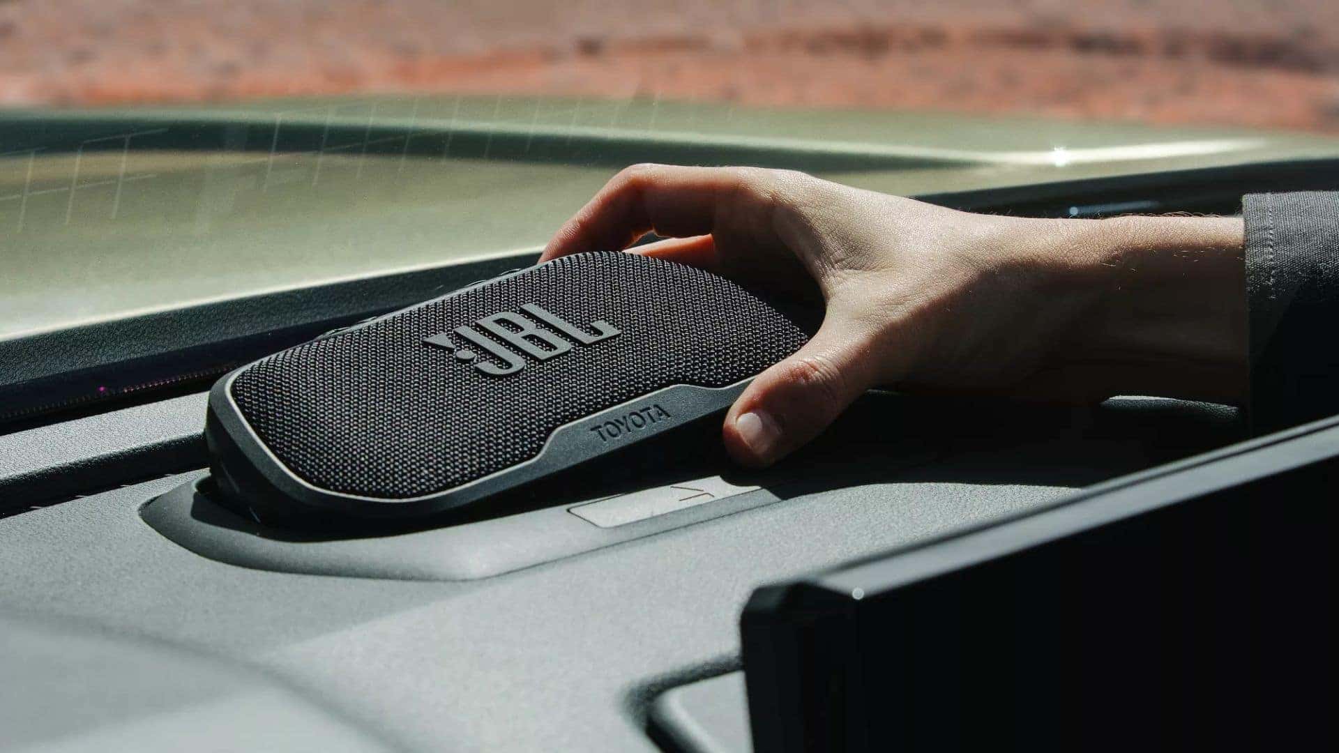 A JBL portable speaker being placed on the dashboard of a Toyota Tacoma, demonstrating premium audio features.