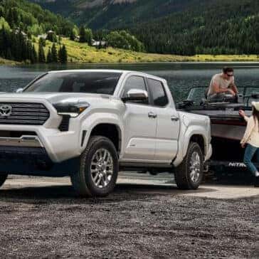 White Toyota Tacoma at a lakeside boat launch with a man securing a fishing boat and a woman assisting.