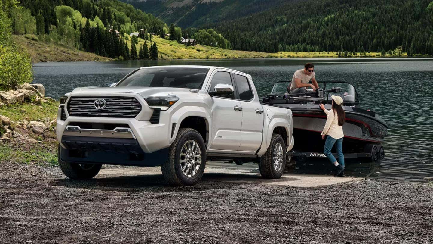 White Toyota Tacoma at a lakeside boat launch with a man securing a fishing boat and a woman assisting.