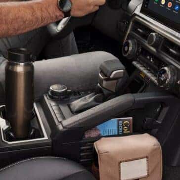 Close-up of the center console in a Toyota Tacoma with a stainless steel travel mug, gear shifter, and a storage slot holding a guidebook.