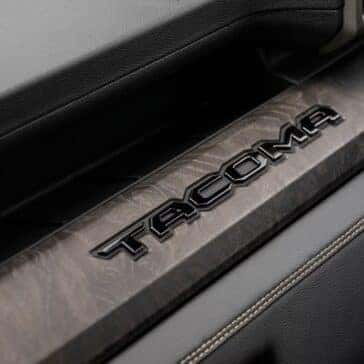 Interior dash detail featuring a 'Tacoma' logo embossed on a wood-accented trim piece.