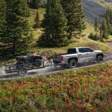 Rear view of a Toyota Tacoma pulling an ATV trailer through a rugged forest trail.