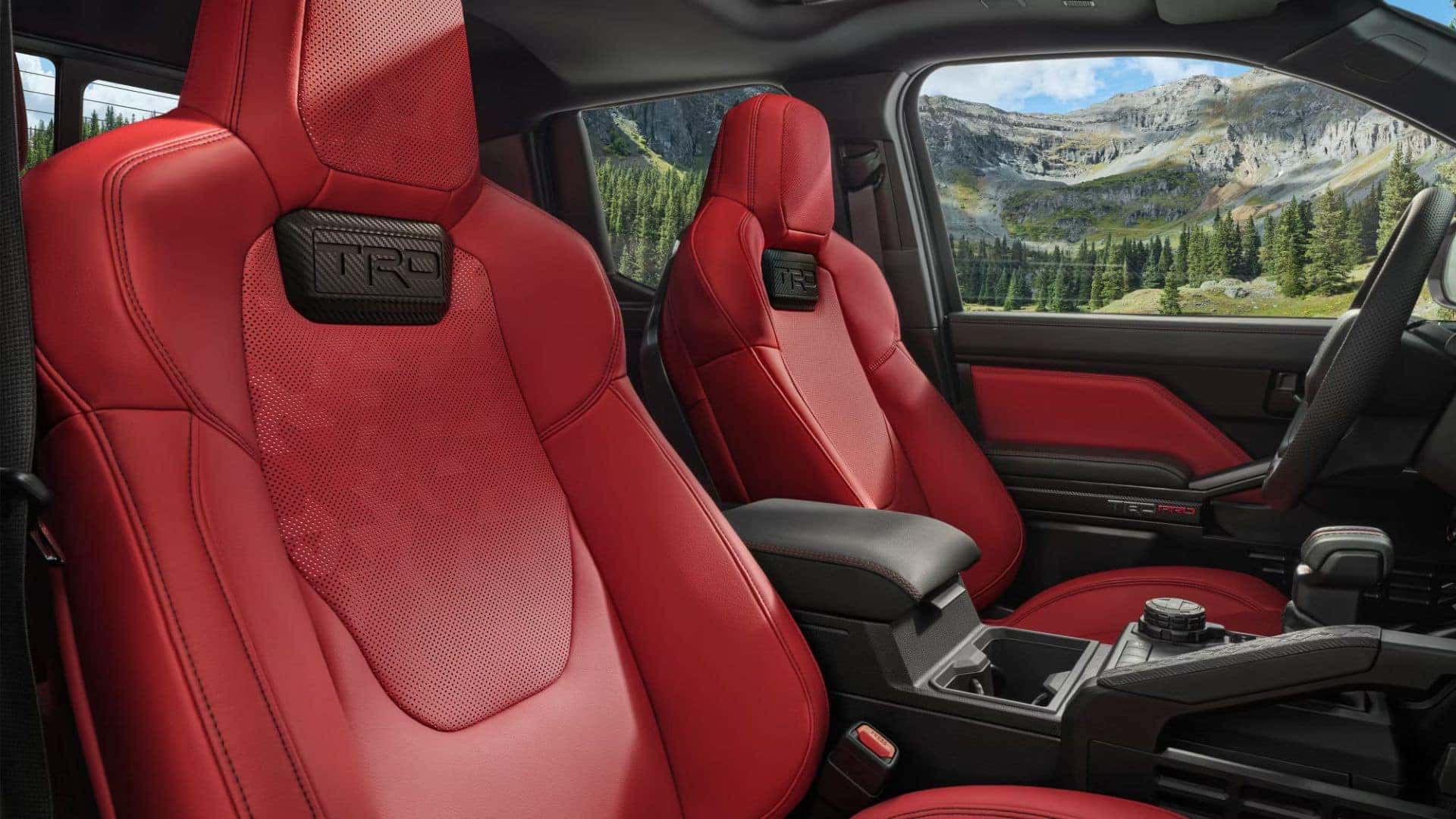 Interior view of a truck with TRD-branded red leather seats and a scenic mountain backdrop through the windows
